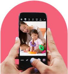 Two hands holding a smart phone taking a picture of a young asian mom and her baby playing with a stacking ring toy